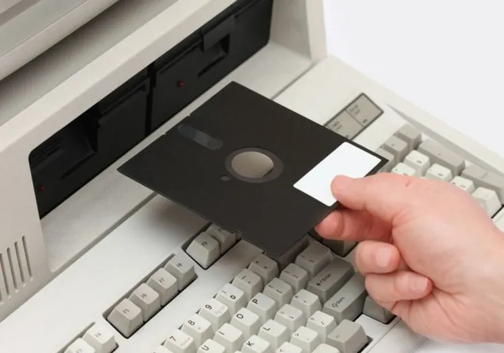 Hand inserting old floppy disk drive into vintage eigthies computer